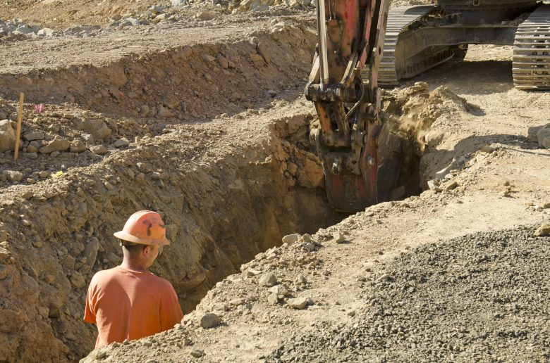 Construction working standing in trench with digger close