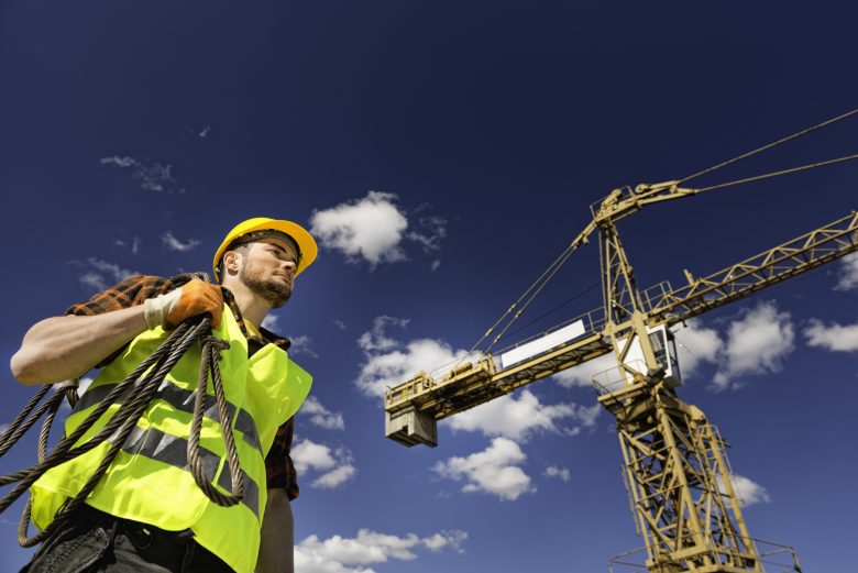 Worker in full PPE walking near a crane on a construction site