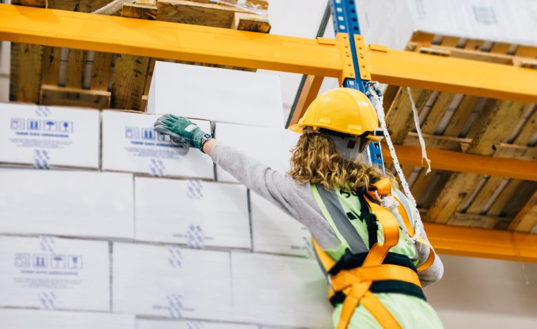 Young female manual worker hanging on a climbing rope in warehouse