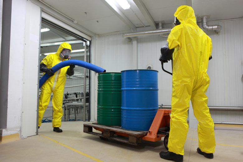 Two specialists in protective uniforms,masks,gloves and boots working with barrels of chemicals in a factory