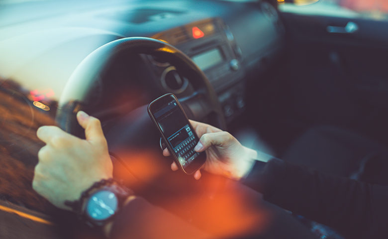 Young businessman driving a car and using smartphone