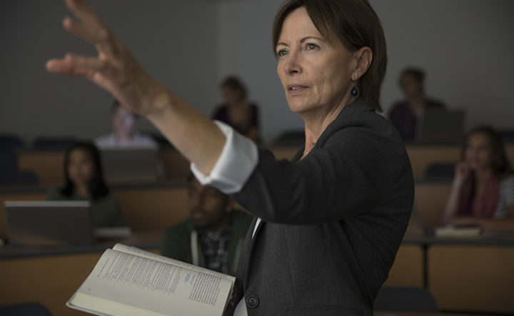 Female professor with textbook teaching lesson in auditorium classroom