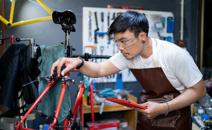 He is using a tablet to check the product. The entrance of the bicycle shop is looking after the customers' bikes for checking the condition.