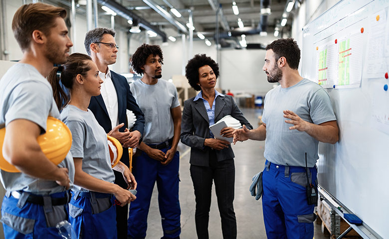 Young worker giving toolbox talk in front of whiteboard in a factory.