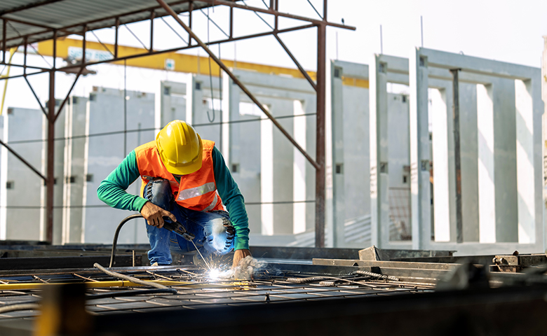 Lone worker at a construction site weld metal structures of precast concrete slabs.